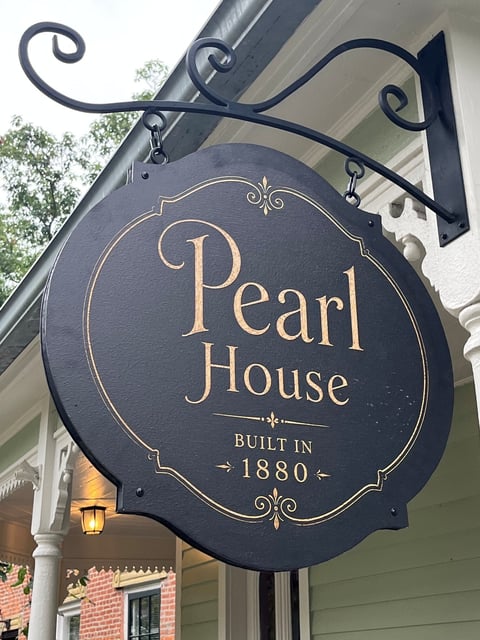 Round black and gold hanging sign for Pearl House with a textured, hand-painted finish